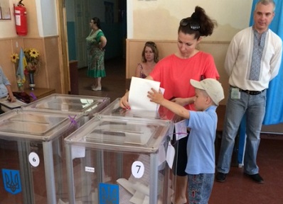 A young boy puts his mother’s ballot in the ballot box.