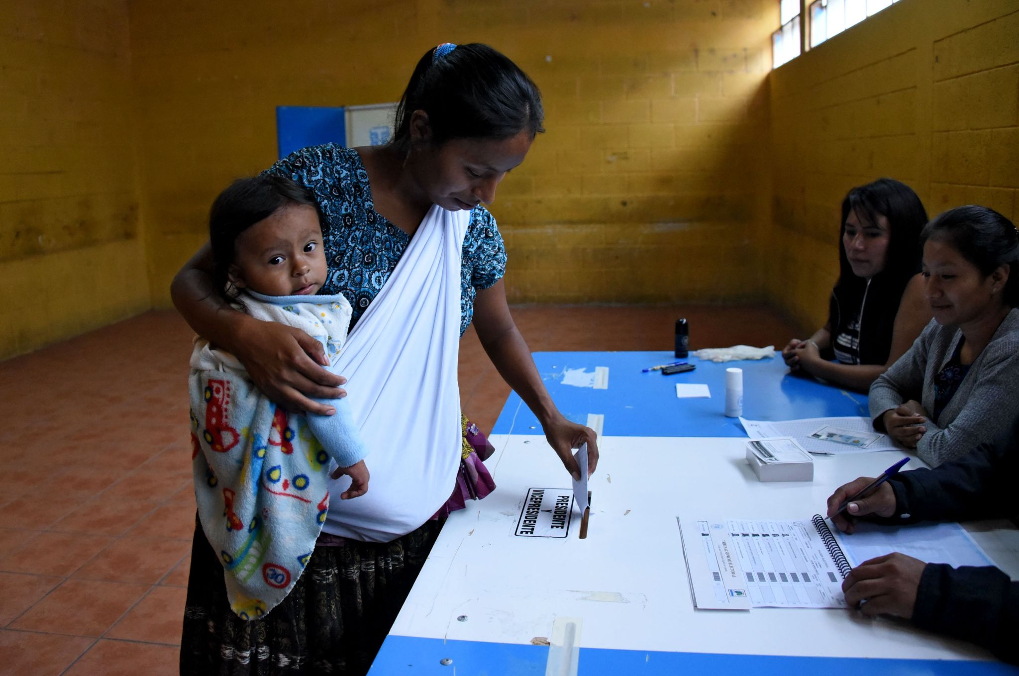 An indigenous woman holding a baby casts her vote