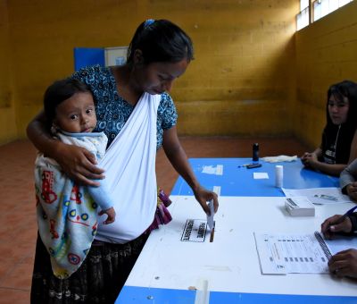 An indigenous woman holding a baby casts her vote