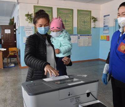 A woman holding a child casts her ballot