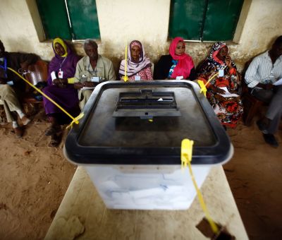 Sudanese election staff sit behind a sealed ballot box