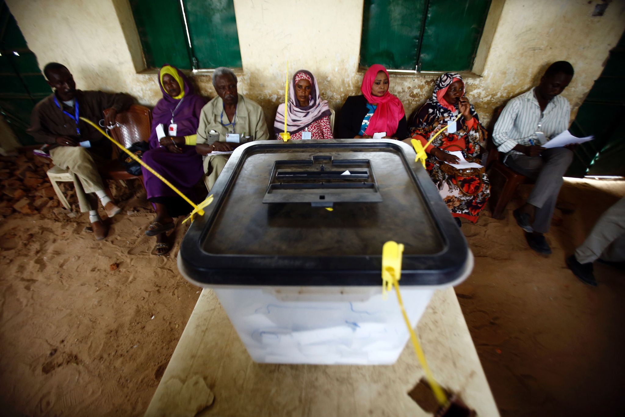 Sudanese election staff sit behind a sealed ballot box