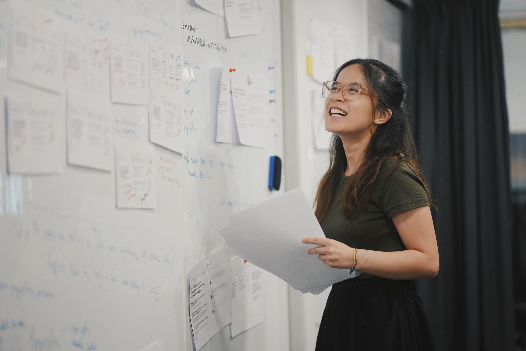 A lady standing at a white board smiling and holding paper