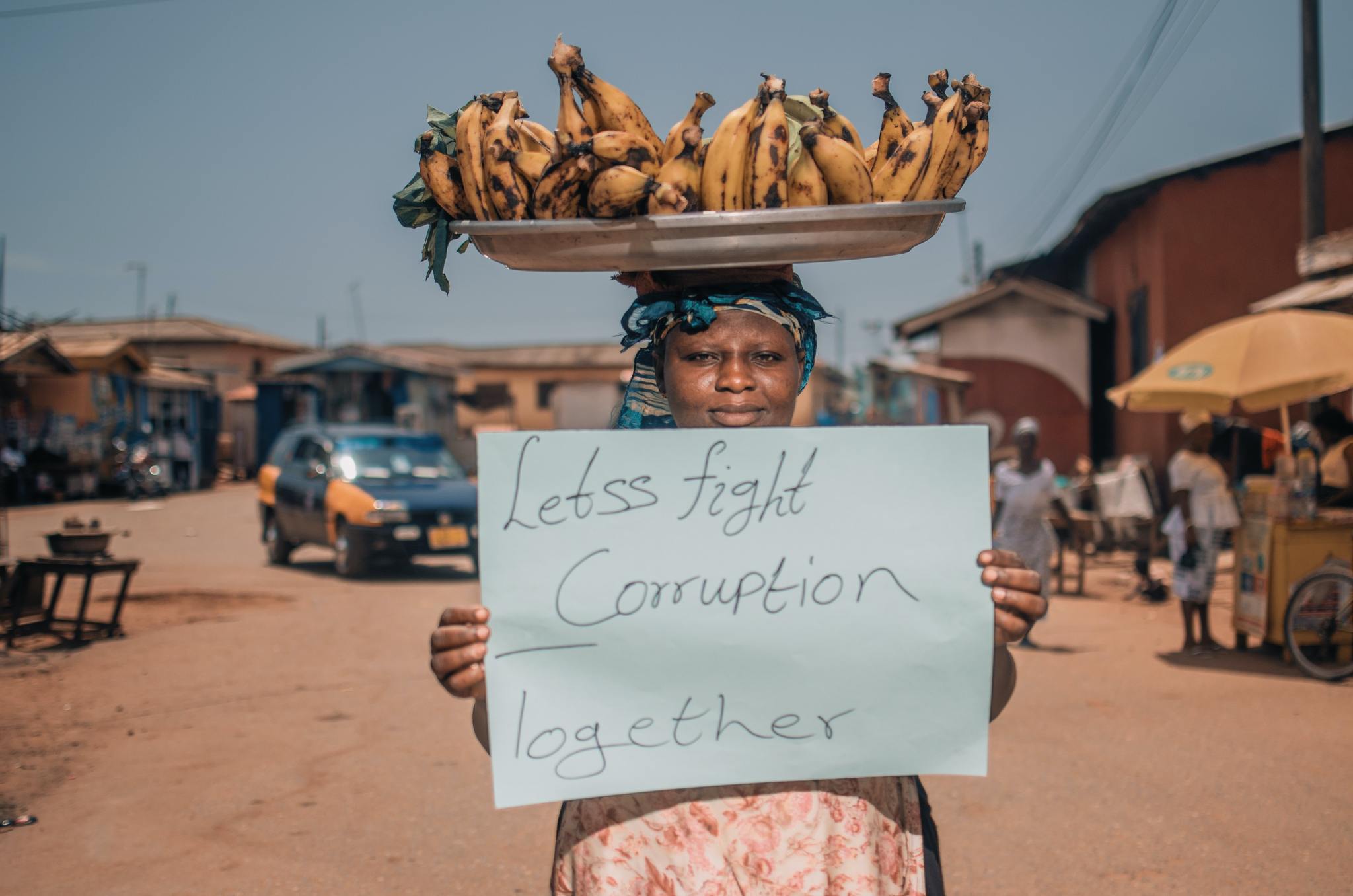 A woman balances bananas on her head and holds up a sign in favor of fighting corruption