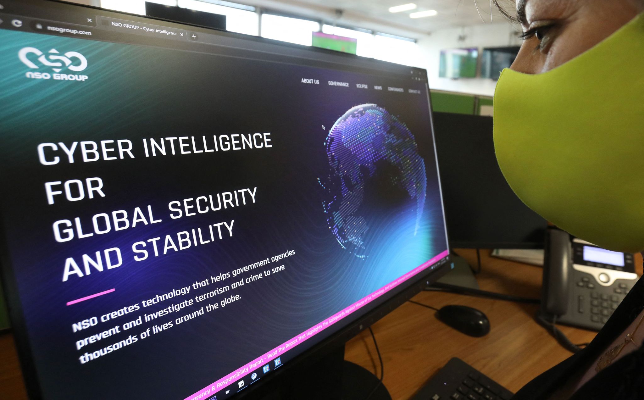 A photo of a woman wearing a mask looking at a computer for cyber intelligence