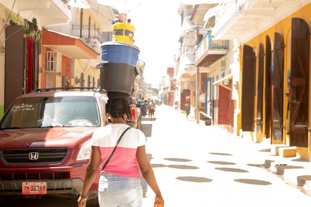 Woman walks down street carrying goods on head