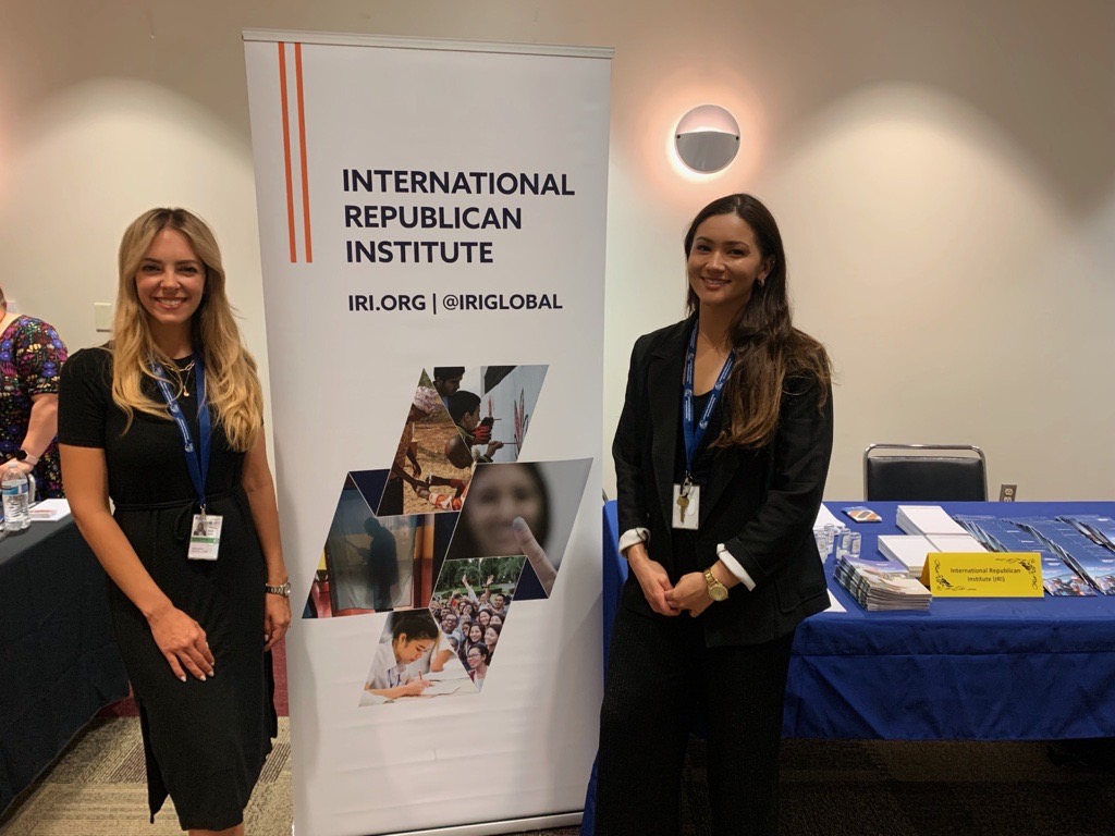 Two IRI Staff Members stand next to IRI Banner
