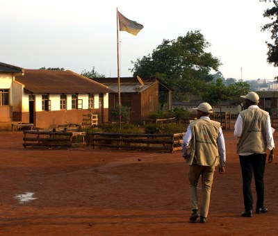 Two men, election observers, walking at sunset in Mozambique. Flag pole in distance.