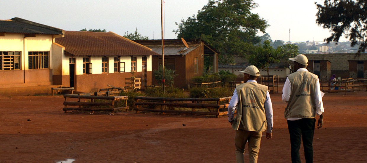 Two men, election observers, walking at sunset in Mozambique. Flag pole in distance.