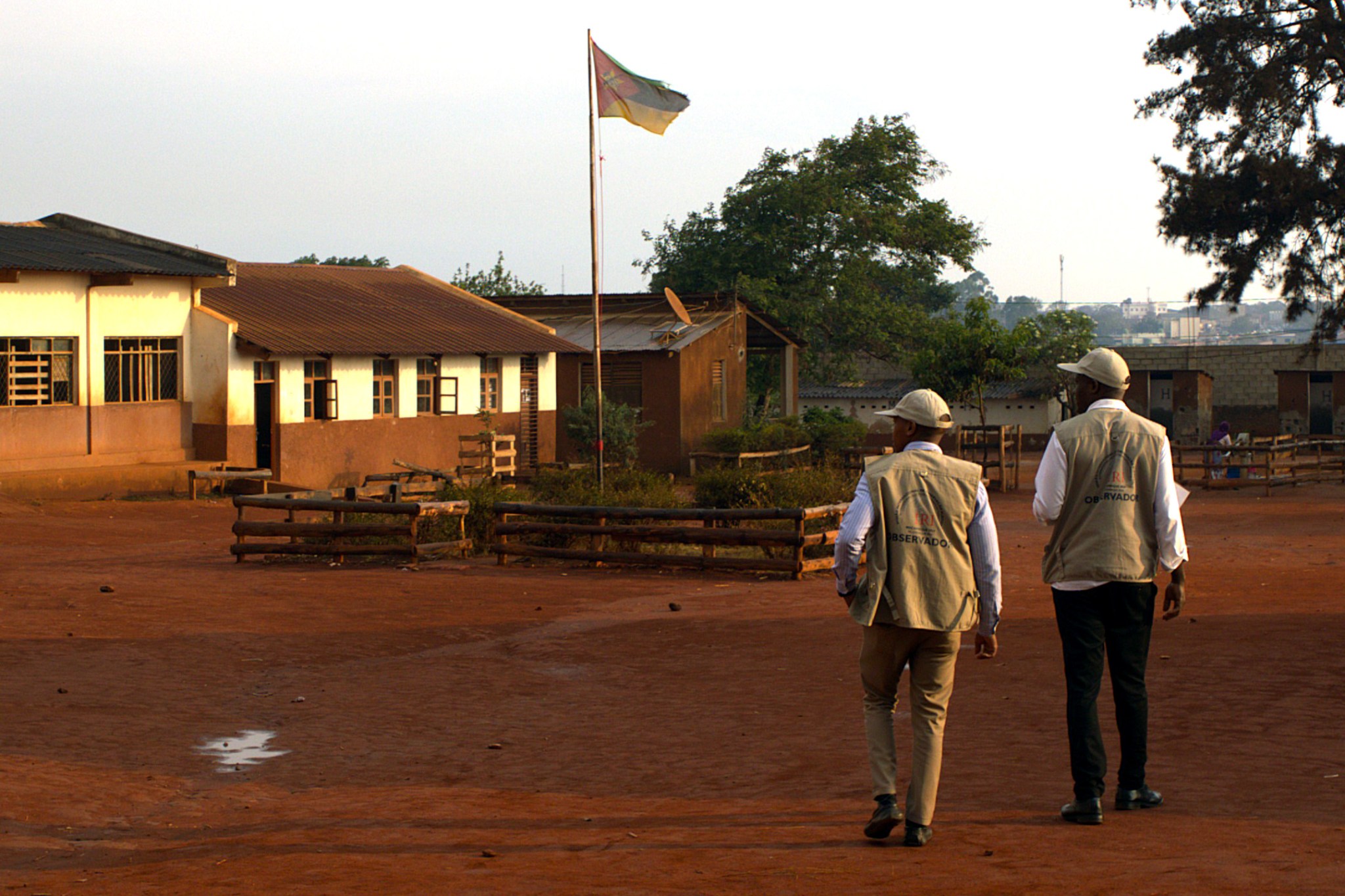 Two men, election observers, walking at sunset in Mozambique. Flag pole in distance.